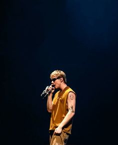 a man standing on top of a stage holding a microphone in his hand and wearing a yellow shirt