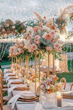 an outdoor dinner table with candles and flowers in vases on the tables, surrounded by string lights