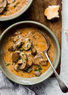 two bowls of soup with mushrooms and parsley on the side, one bowl is full of soup