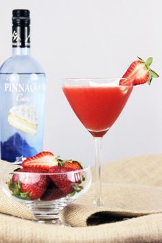 a strawberry martini next to a bottle of ginzaccino and a bowl of strawberries