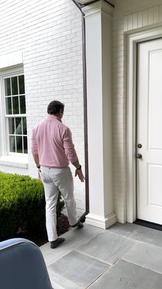 a man in pink shirt and white pants standing next to a door with his foot on the ground