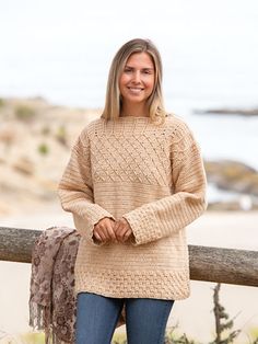 a woman standing next to a wooden fence near the ocean with her hands on her hips