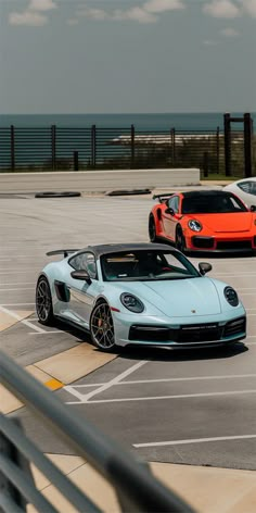 three different colored sports cars parked in a parking lot next to each other with the ocean in the background