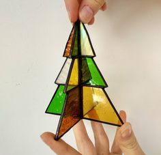 a hand holding a stained glass christmas tree ornament