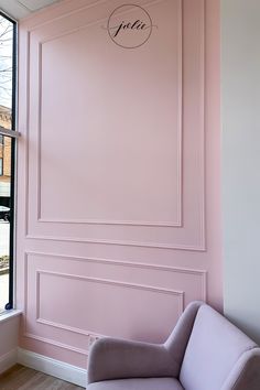 a pink room with a gray chair in front of the window and a sign on the wall