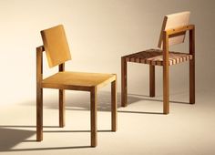 two wooden chairs sitting next to each other on a white surface in front of a gray background