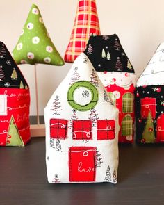 small houses made out of fabric sitting on a table next to christmas trees and ornaments