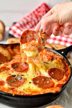 a person is lifting a piece of pizza from a skillet with cheese and pepperoni