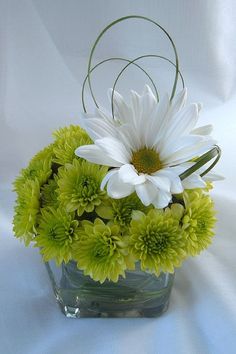 a vase filled with green and white flowers on top of a white cloth covered table