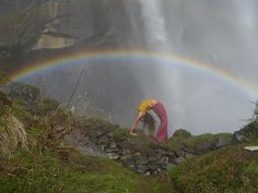 a woman bending over in front of a waterfall with a rainbow coming out of it