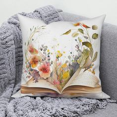 an open book with flowers on it sitting on a couch next to a throw pillow