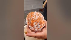 a person holding a powdered sugar donut in their hand, with the doughnut being held up