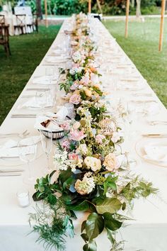 a long table is set up with flowers and greenery for an outdoor wedding reception