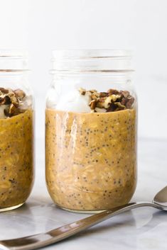 two jars filled with oatmeal and nuts on top of a table next to a spoon