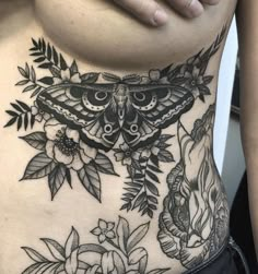 a woman's stomach with a butterfly and flowers tattoo on her side, which is surrounded by leaves