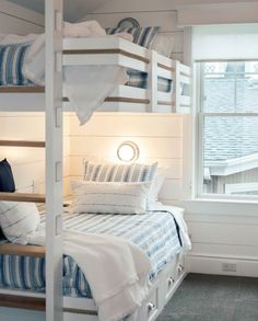 bunk beds with blue and white bedding in a small room next to a window