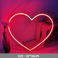 a heart shaped neon sign sitting on top of a table next to a vase with flowers