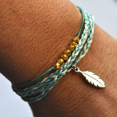 a close up of a person's arm wearing a bracelet with a feather charm