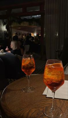 two glasses filled with liquid sitting on top of a wooden table in front of people