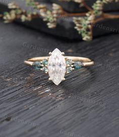 an engagement ring with a pear shaped diamond surrounded by blue and green stones on a wooden surface