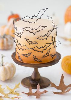 a decorated cake sitting on top of a wooden stand next to pumpkins and leaves