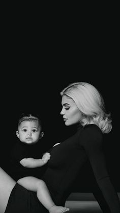 a woman holding a baby in her lap while posing for the camera with black background