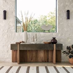 a table with two vases on it in front of a window and a rug