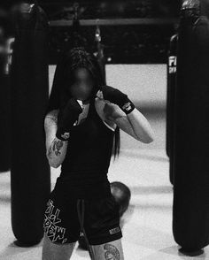 a woman with tattoos on her arm standing in a boxing ring next to punching bags