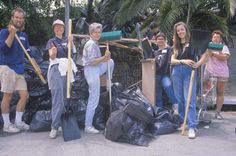 group of people holding shovels and bags in front of trash bins with palm trees behind them