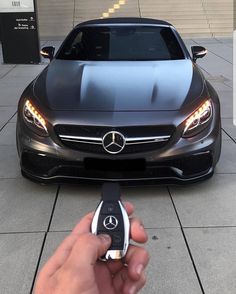 a person holding a remote control in front of a mercedes benz car on the street