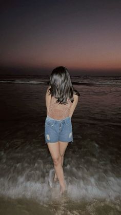 a woman standing in the ocean at night with her back turned to the camera and looking into the water