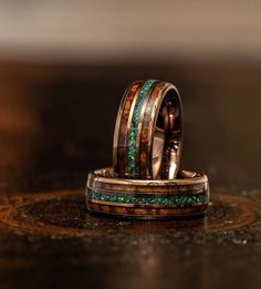 two wedding bands with green and brown wood inlays on top of each other