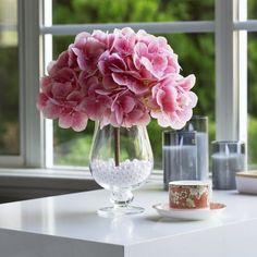 a glass vase with pink flowers in it on a table next to a cup and saucer