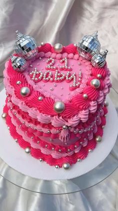 a heart shaped birthday cake with pink frosting and silver decorations on top, sitting on a white plate