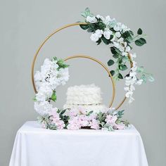 a white cake with flowers and greenery sits on a table in front of a circular frame