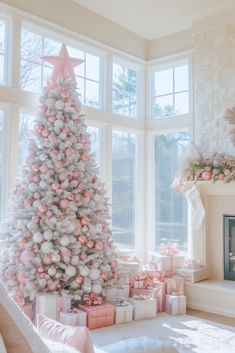 a white christmas tree with pink and silver ornaments in front of a large window filled with presents