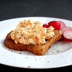 a white plate topped with toasted bread covered in cheese and veggies next to sliced radishes