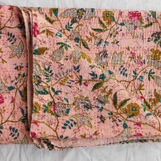 an old pink blanket with flowers and leaves on it, sitting on a white sheet