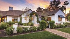 a white brick house with landscaping and trees in the front yard at sunset or dawn