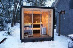 an outdoor sauna in the snow next to a building with its doors open and lights on