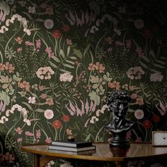 a table with a clock on top of it next to a wallpaper covered in flowers