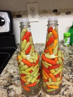 two glass bottles filled with pickles and carrots on top of a granite counter