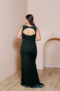 a woman in a dark green dress standing on a wooden floor with her back to the camera