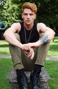 a young man sitting on top of a stone bench wearing black shoes and holding his hands in his pockets