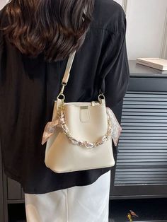 a woman holding a white purse with a chain around the strap and an attached pouch