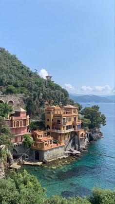 some buildings on the side of a cliff by the water with trees and bushes around them