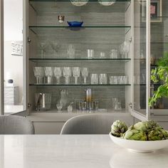 a bowl of artichokes sits on a table in front of glass shelves