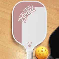 a pickleball paddle next to a black case on a wooden table with an orange ball