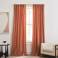 an orange curtain hangs in front of a window with a white chair and side table