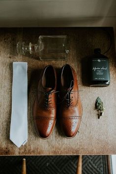 a pair of brown shoes sitting on top of a wooden table next to a white tie